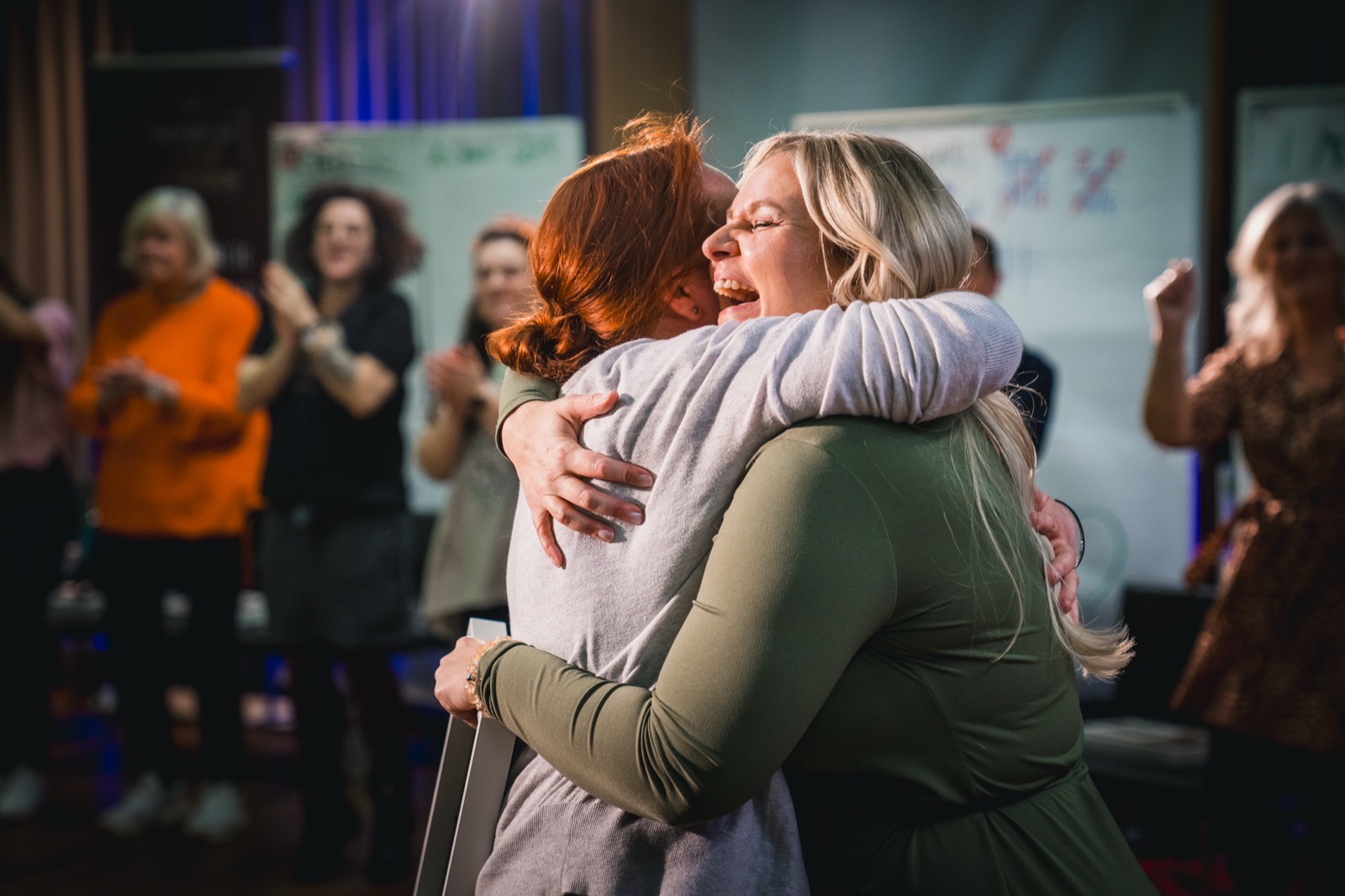 Zwei Frauen umarmen sich im Workshop, andere applaudieren